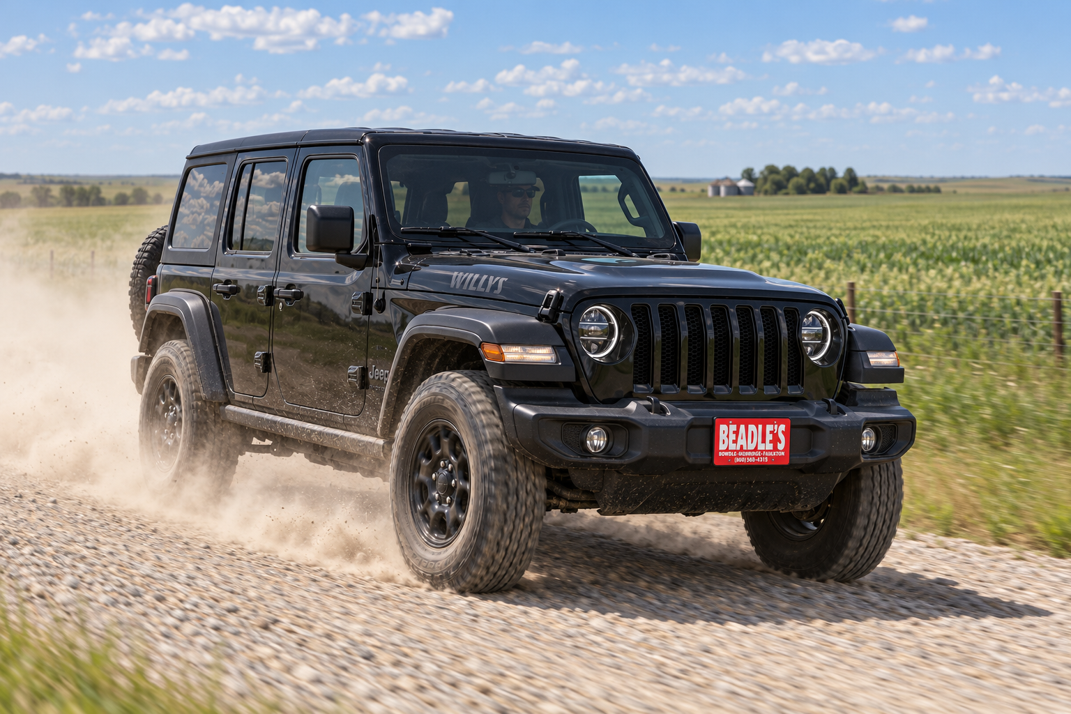 Black 2026 Jeep Wrangler Willys kicking up dust on a South Dakota gravel road, at Beadle's Chrysler Center